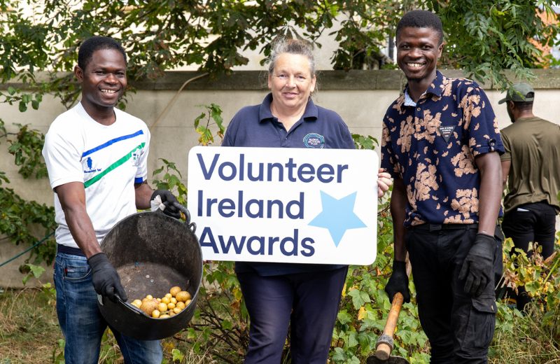 a smiling man holding potatoes, a smiling woman holding a sign reading volunteer ireland awards and a smiling man holding a gardening tool