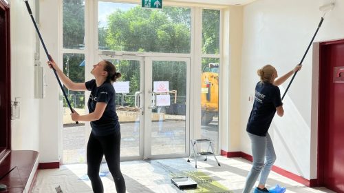 two people with long painting rollers paint the entrance hall to a building