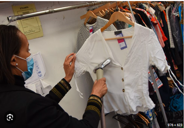 a woman in a mask steams a shirt hanging on a rack