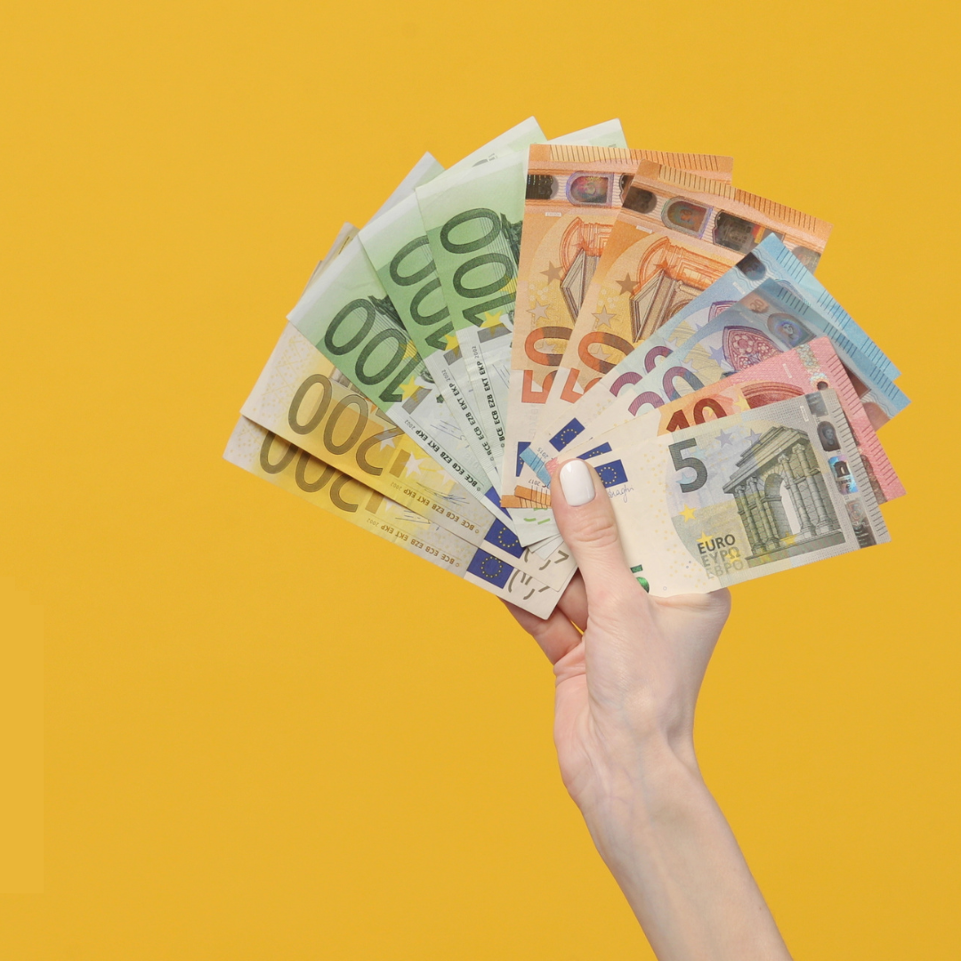 a hand with painted nails holds euro bills on a bright yellow background